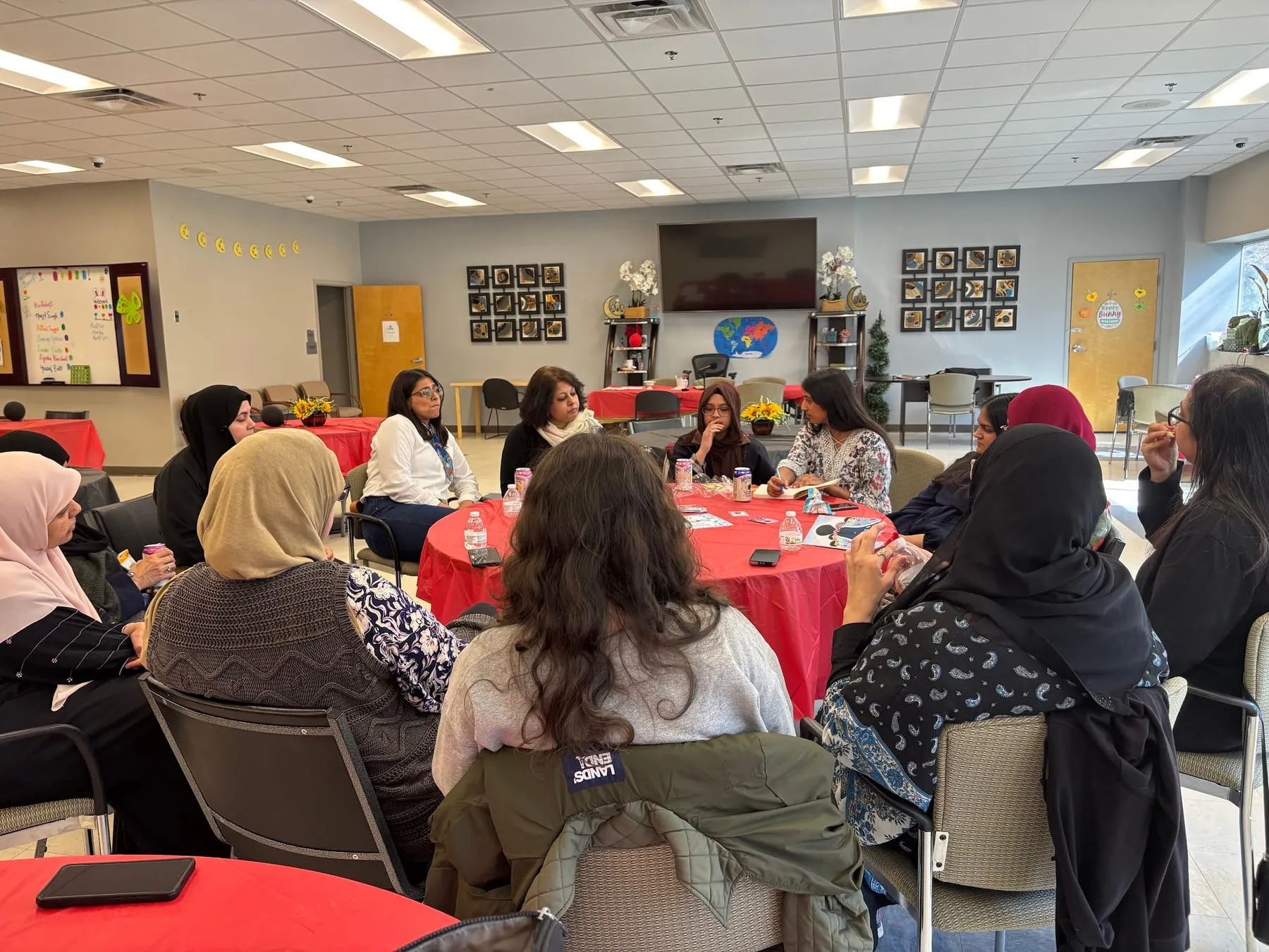 A hall of women at red-clothed tables playing Rishta at a Give Her Space session
