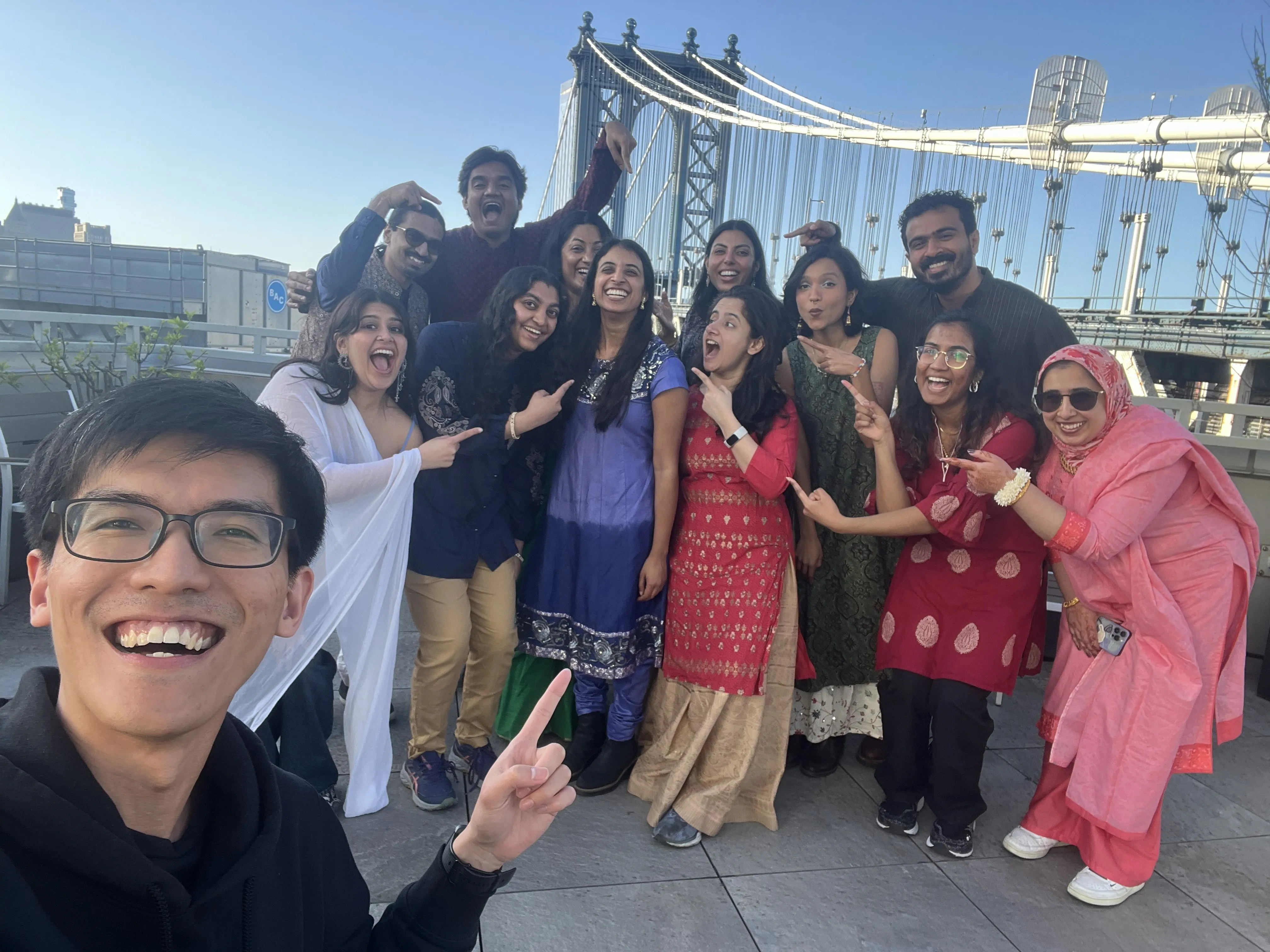 The photoshoot crew on a rooftop in front of the Manhattan Bridge, everyone pointing at the game designer
