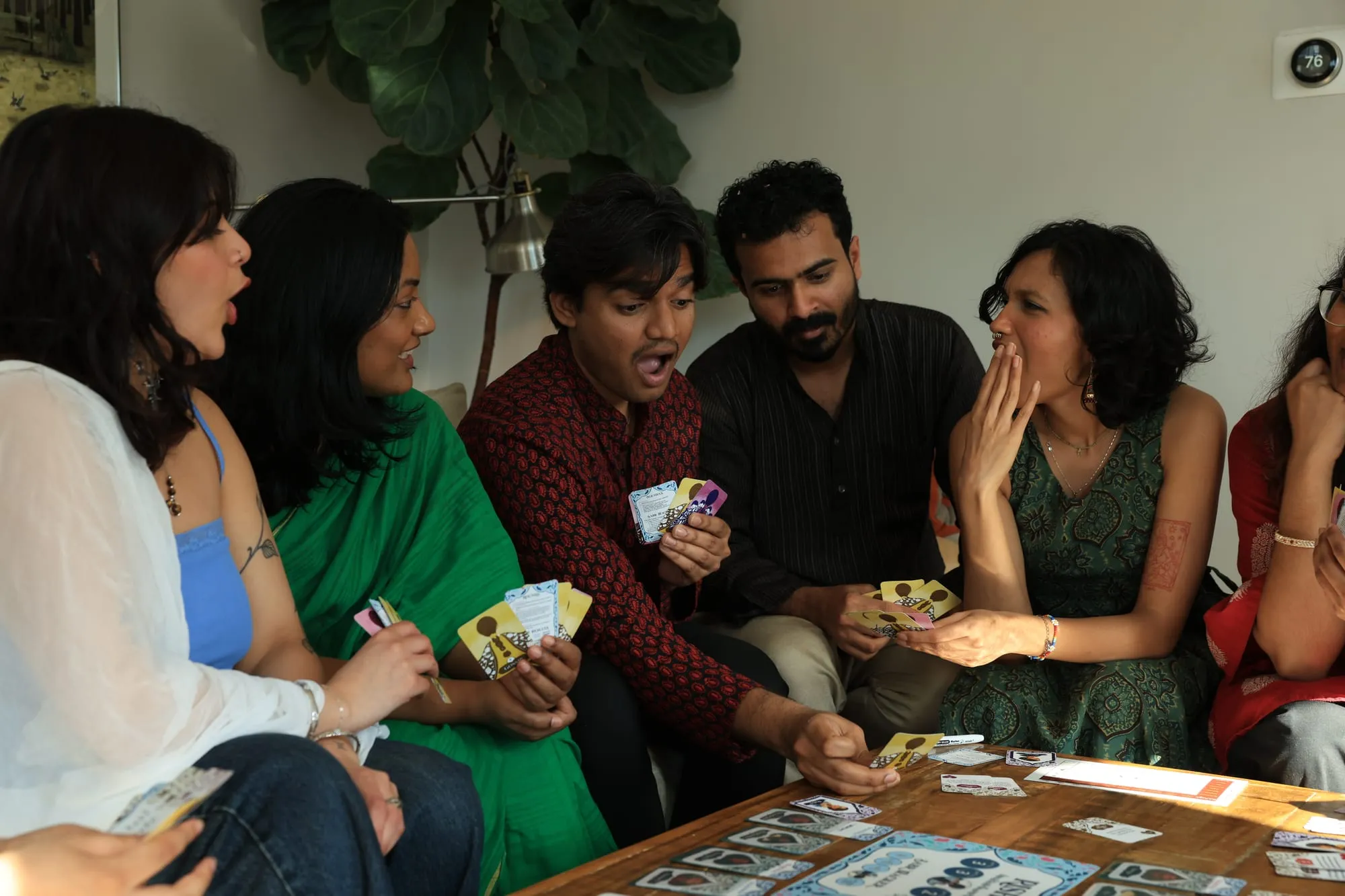 A player at a low table laughing behind her cards while the others watch