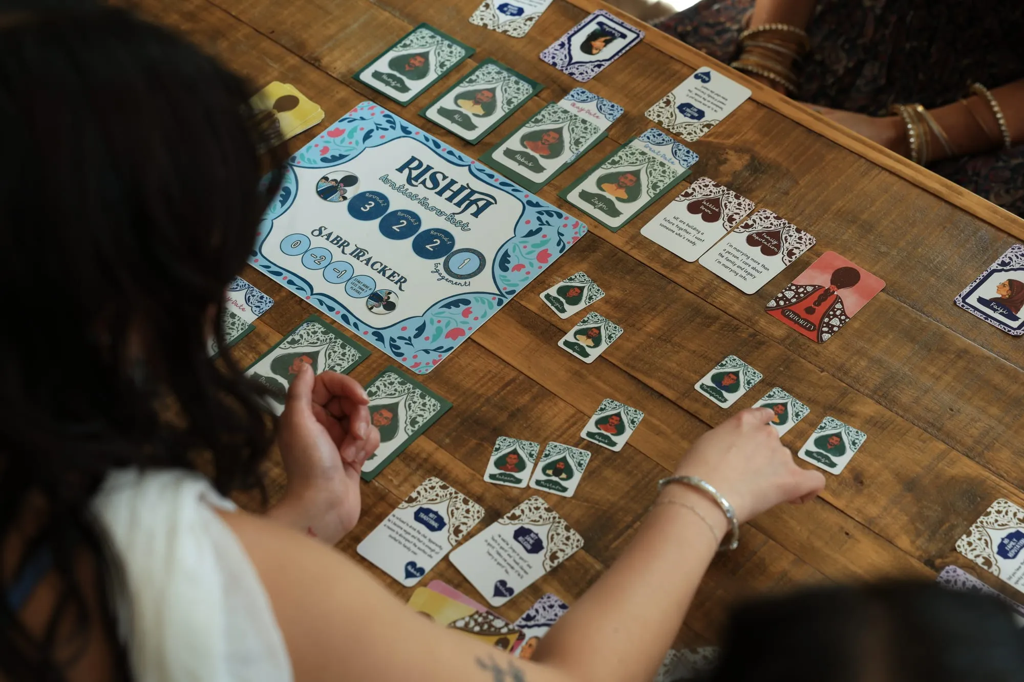 An overhead view of the board and suitor cards, a hand reaching across
