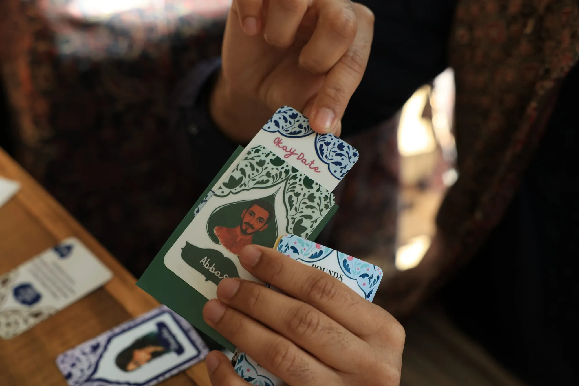 A hand lifting a suitor card to show the result card tucked behind it