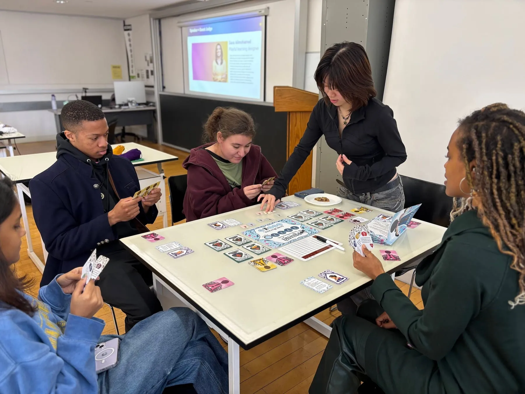 Students around a table in a Pratt classroom, a projector lit behind them