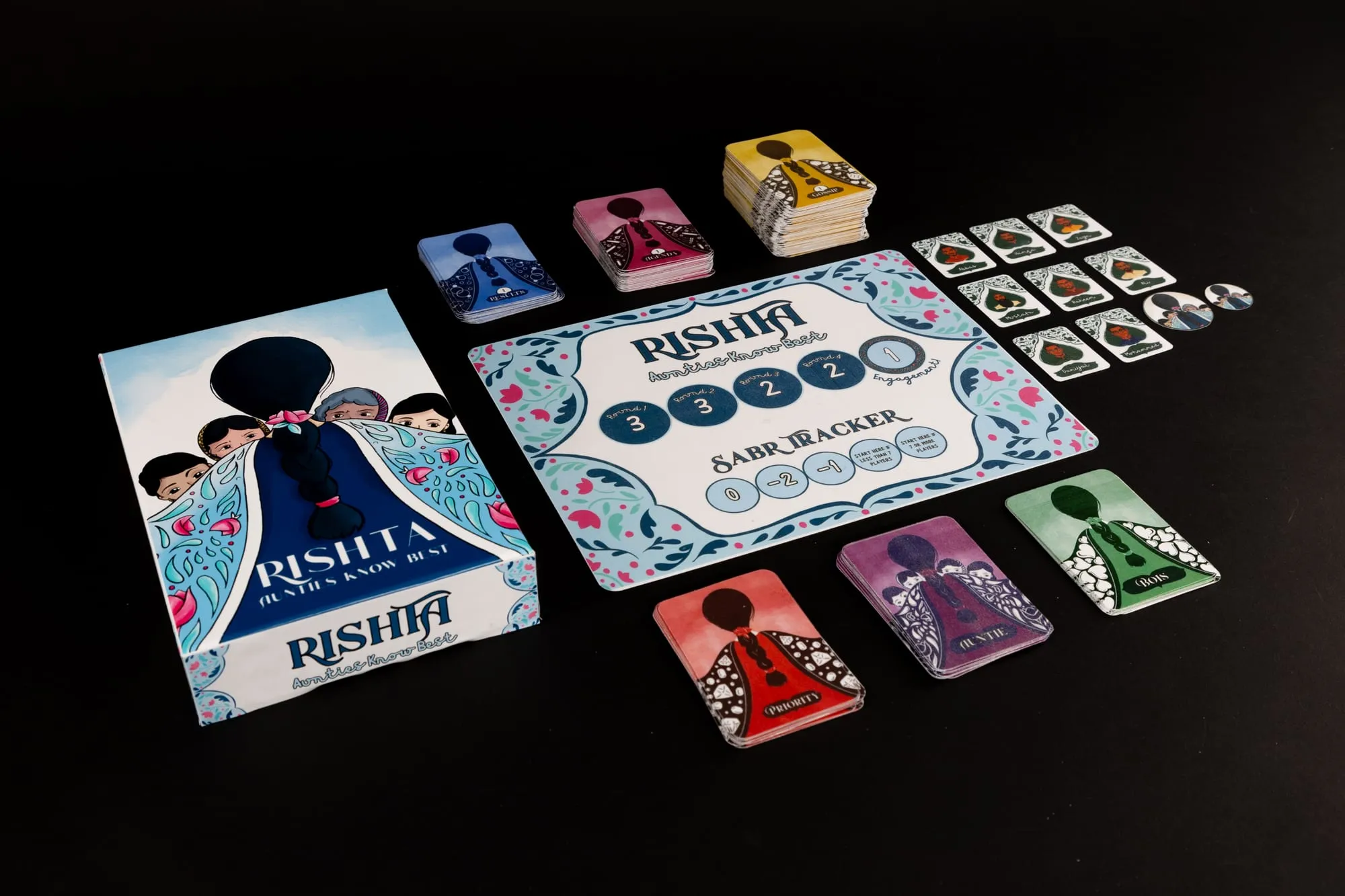 The Rishta box, board, suitor cards and token stacks laid out on black